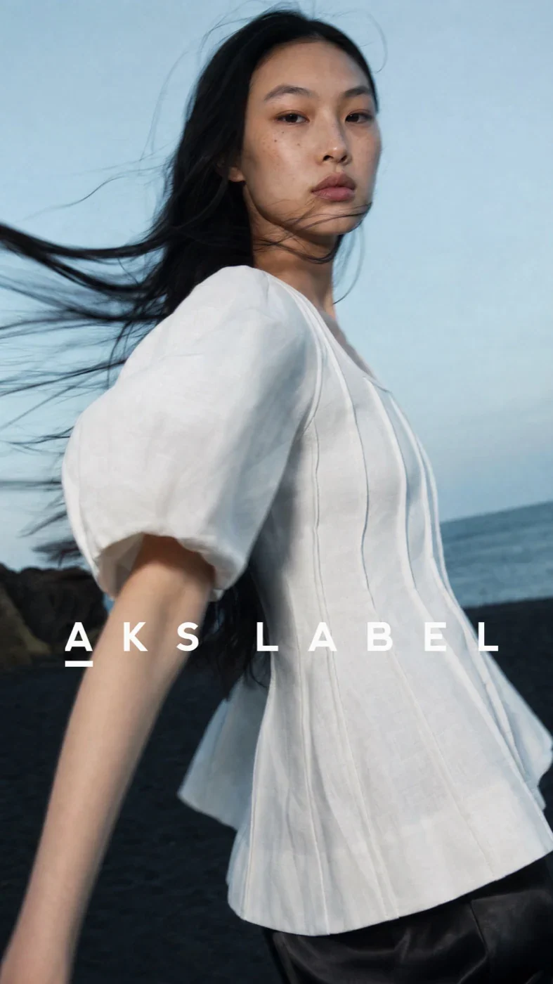 AKS Label model in a white blouse against a blue sky