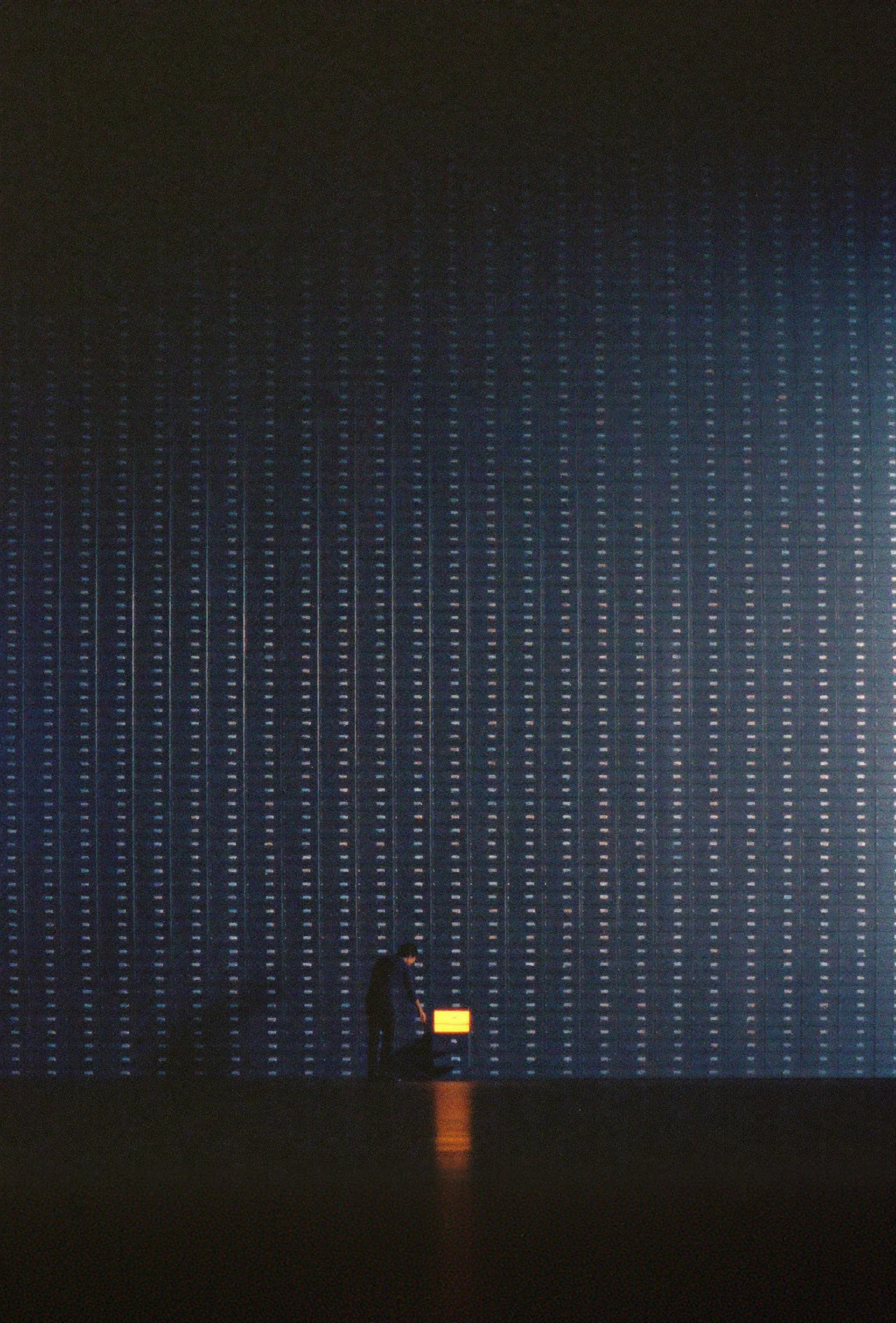 A lone figure facing a towering wall of archive drawers